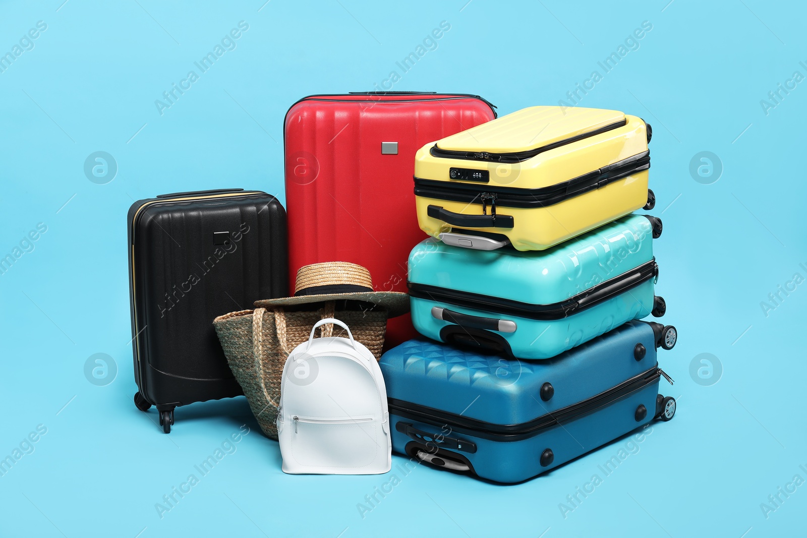 Photo of Colorful suitcases, backpack, beach bag and straw hat on light blue background