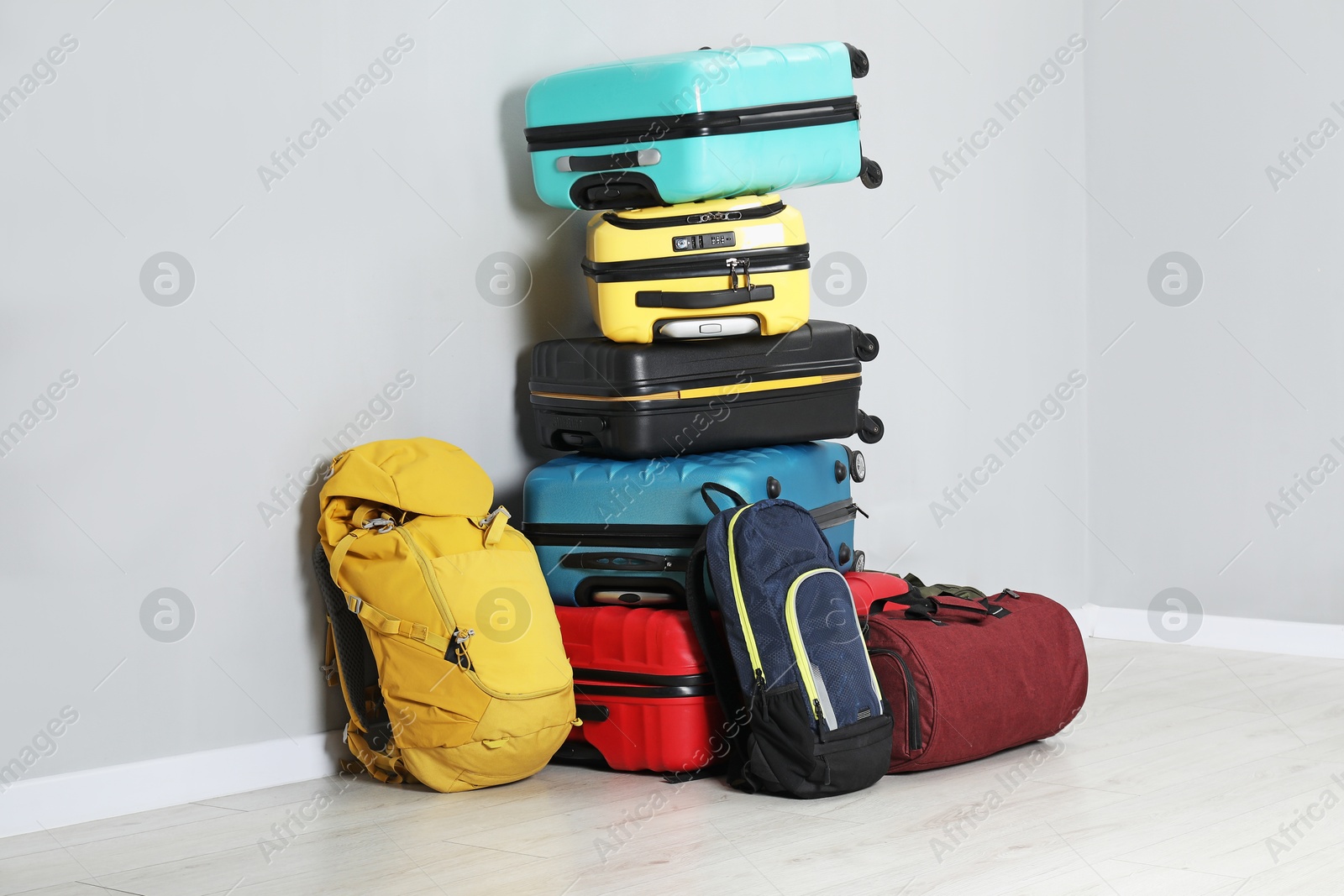 Photo of Stack of colorful suitcases, backpacks and bag on floor near light wall