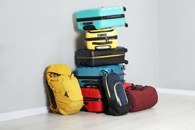 Photo of Stack of colorful suitcases, backpacks and bag on floor near light wall