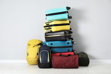 Photo of Stack of colorful suitcases, backpacks and bags on floor near light wall