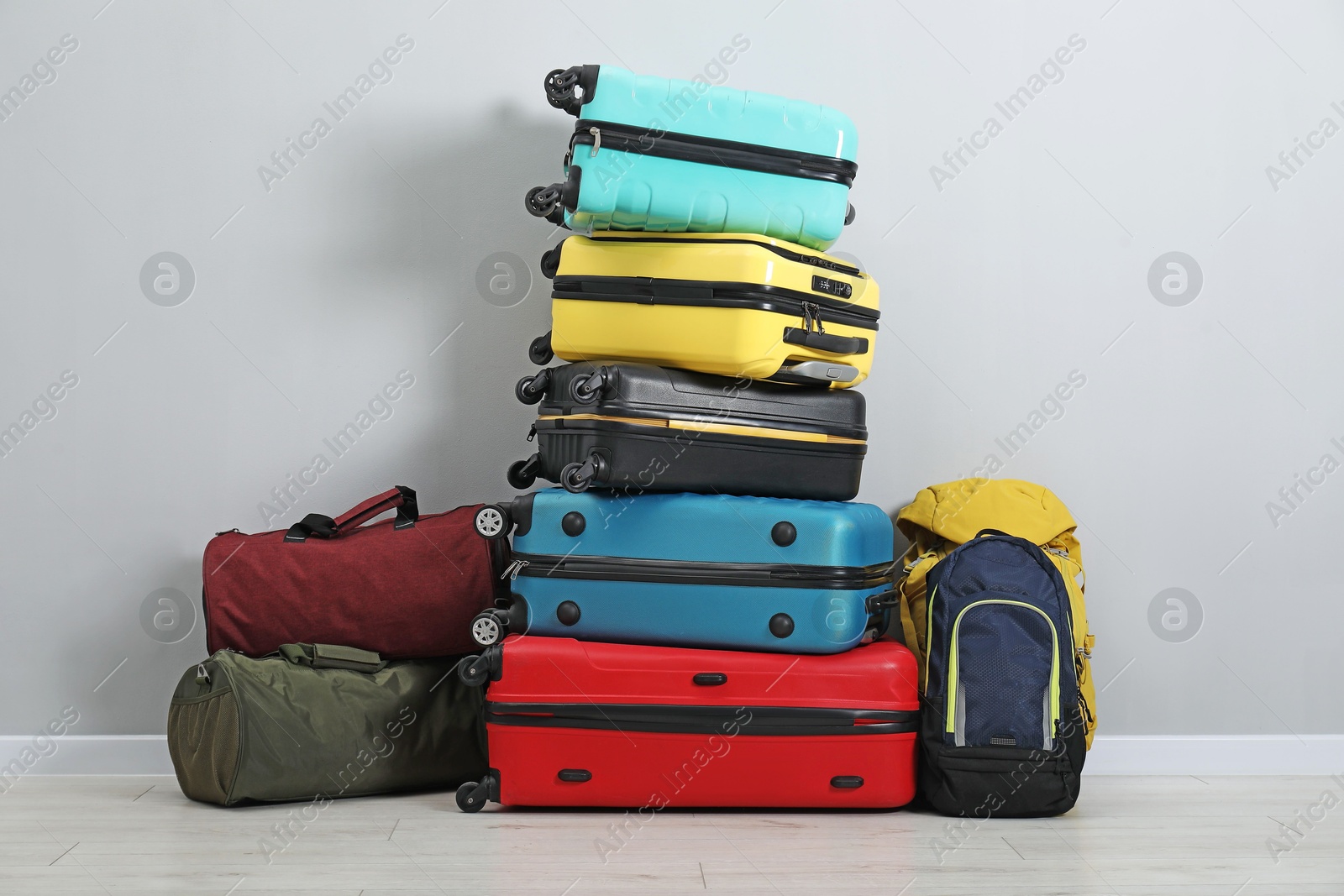 Photo of Stack of colorful suitcases, backpacks and bags on floor near light wall