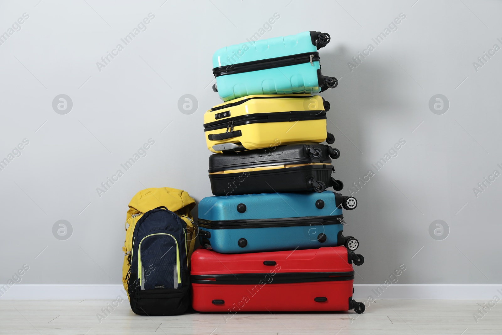 Photo of Stack of colorful suitcases and backpacks on floor near light wall