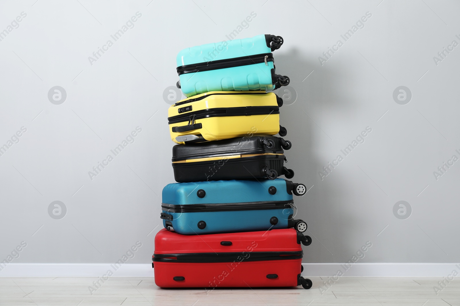 Photo of Stack of colorful suitcases on floor near light wall