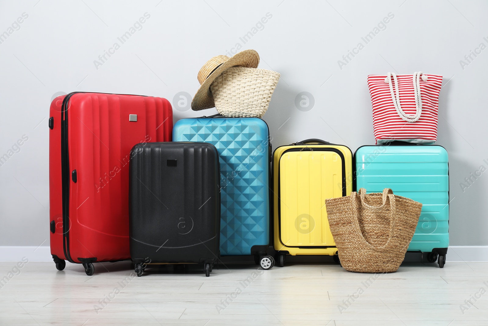 Photo of Colorful suitcases, beach bags and straw hat on floor near light wall