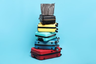 Photo of Stack of colorful suitcases and bag on light blue background