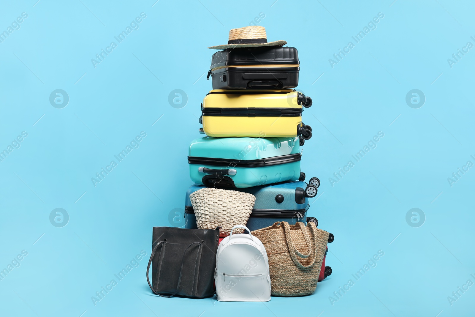 Photo of Stack of colorful suitcases, backpack, bags and hat on light blue background