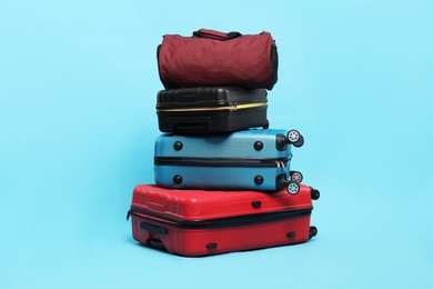 Photo of Stack of colorful suitcases and bag on light blue background