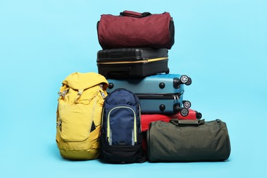 Photo of Stack of colorful suitcases, backpacks and bags on light blue background