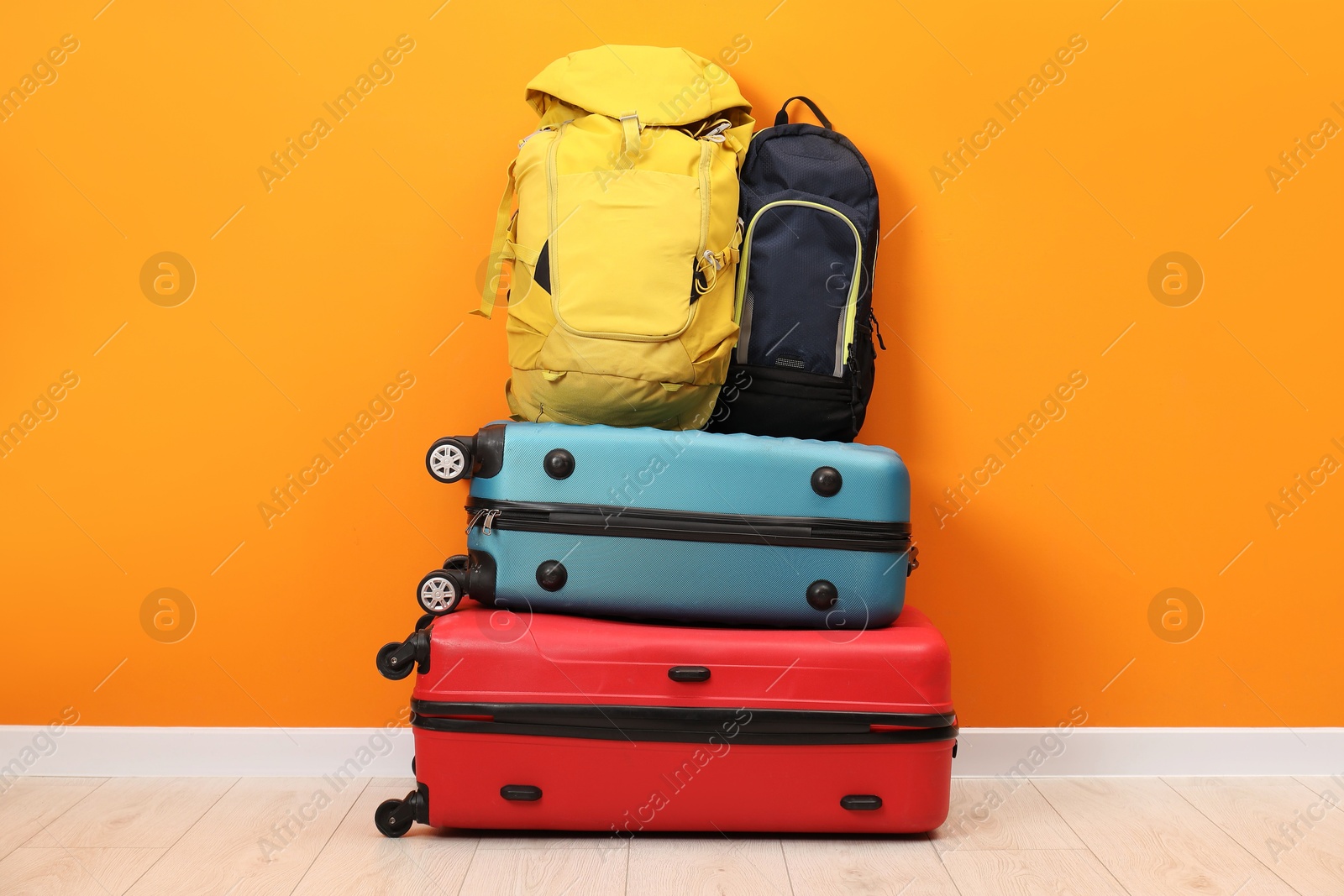 Photo of Stack of colorful suitcases and backpacks on floor near orange wall