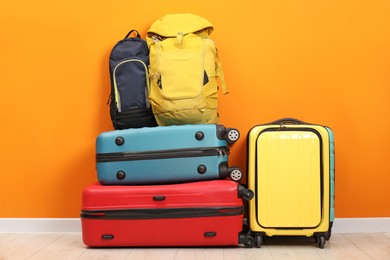 Photo of Many colorful suitcases and backpacks on floor near orange wall