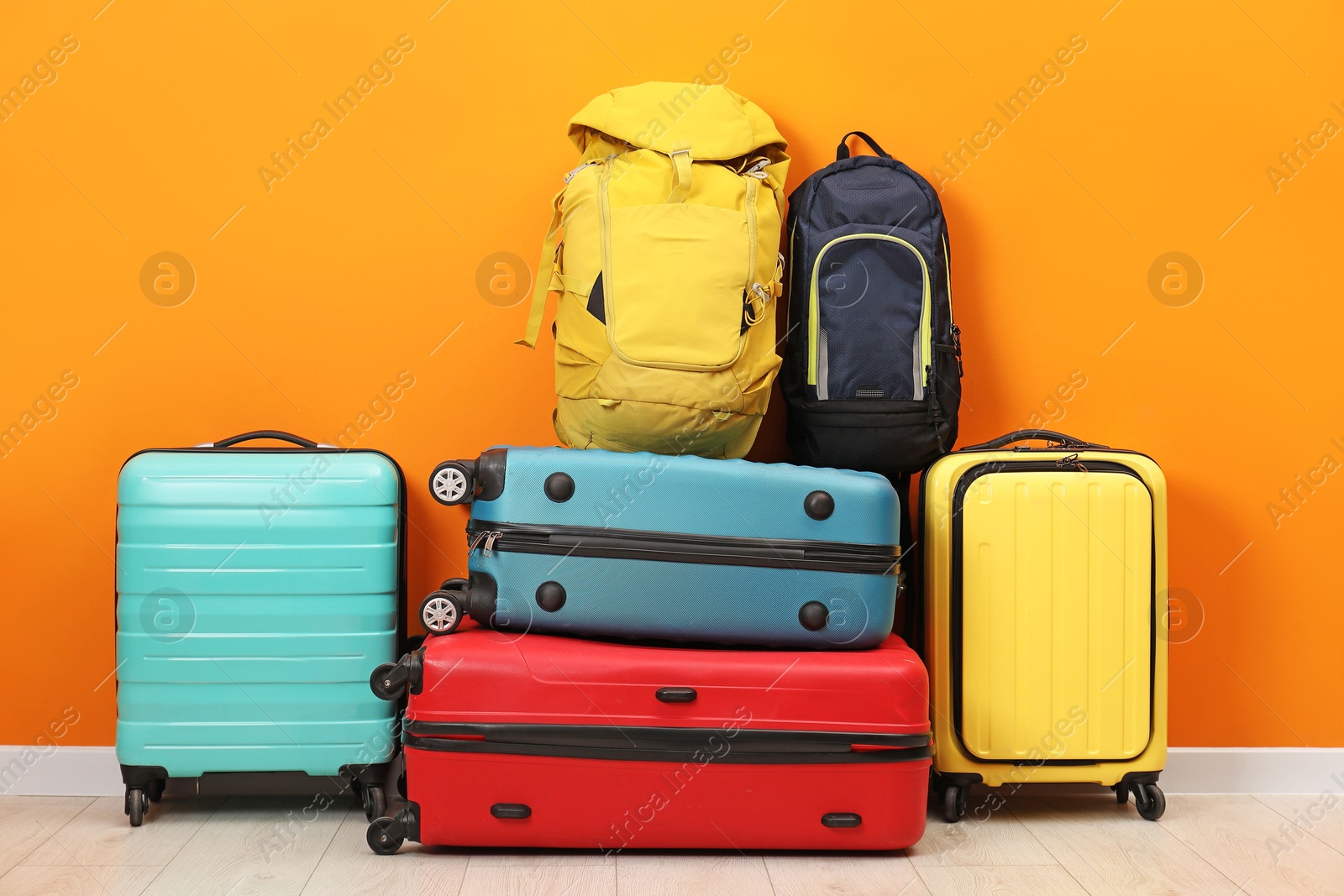 Photo of Many colorful suitcases and backpacks on floor near orange wall