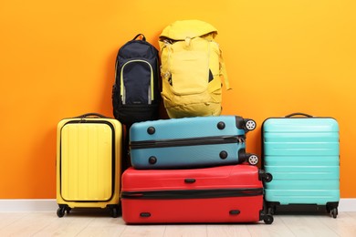 Photo of Many colorful suitcases and backpacks on floor near orange wall