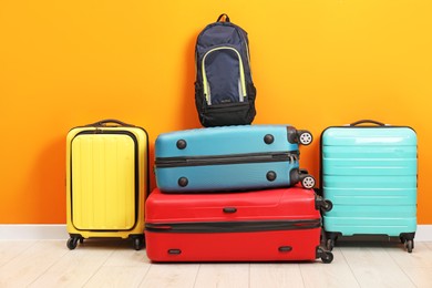 Many colorful suitcases and backpacks on floor near orange wall