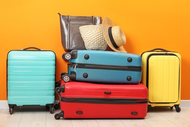 Many colorful suitcases, beach bags and hat on floor near orange wall