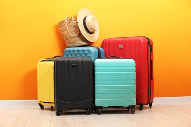 Photo of Many colorful suitcases, beach bag and hat on floor near orange wall