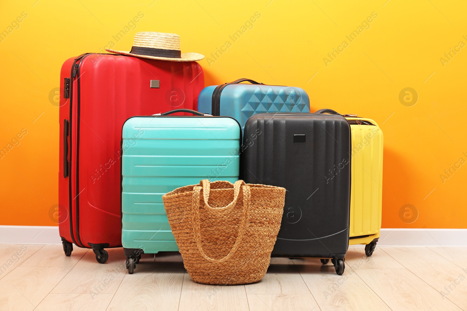 Photo of Many colorful suitcases, beach bag and hat on floor near orange wall