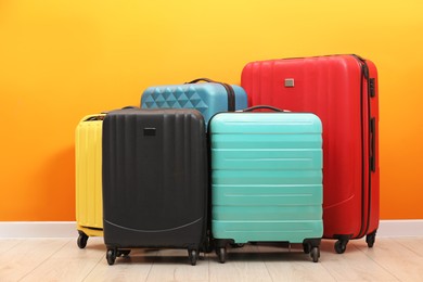 Photo of Many colorful suitcases on floor near orange wall