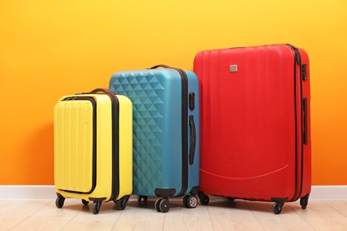 Photo of Many colorful suitcases on floor near orange wall