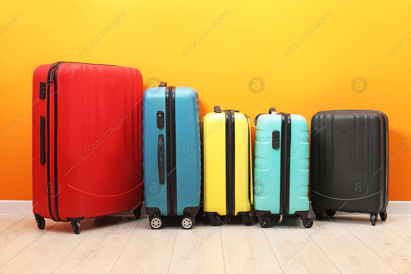 Photo of Many colorful suitcases on floor near orange wall