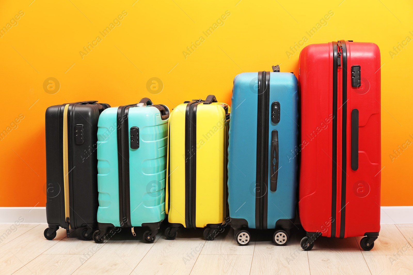 Photo of Many colorful suitcases on floor near orange wall