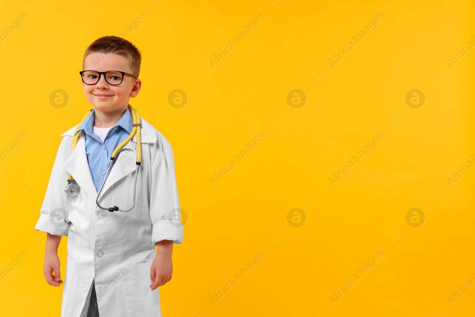 Photo of Little boy with stethoscope pretending to be doctor on yellow background, space for text. Dreaming of future profession