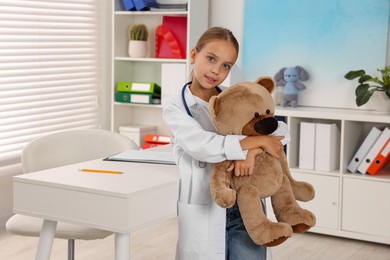 Photo of Girl with stethoscope and toy pretending to be doctor indoors