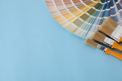 Photo of Color selection charts and paint brushes on light blue table, space for text. Decorating and design