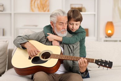 Grandpa teaching his grandson to play guitar on sofa at home