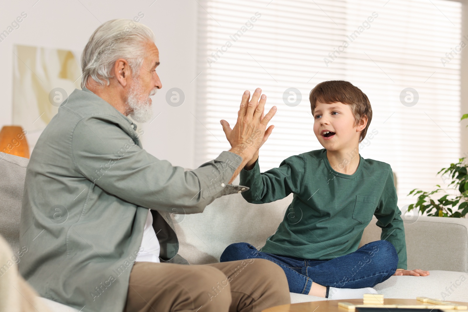 Photo of Grandpa and his grandson giving five on sofa at home