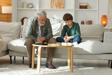 Grandpa and his grandson playing dominoes at table indoors