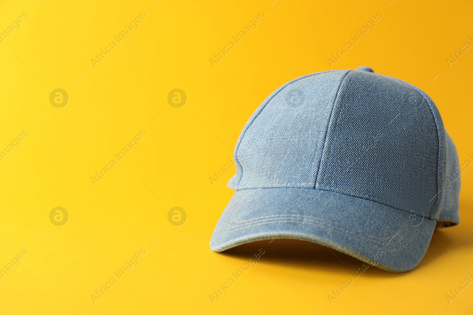 Photo of Stylish denim baseball cap on yellow background. Mockup for design