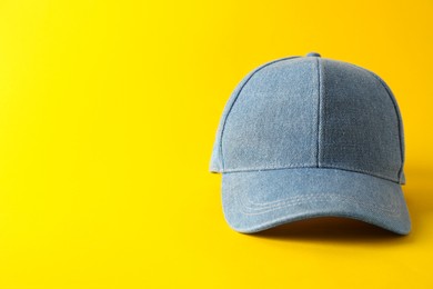 Photo of Stylish denim baseball cap on yellow background. Mockup for design