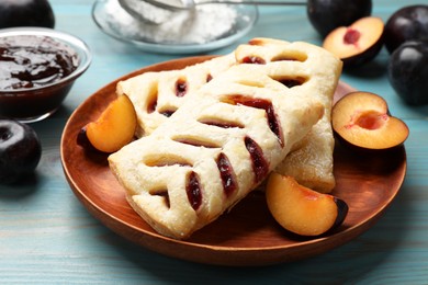 Photo of Delicious puff pastries and plums on light blue wooden table, closeup