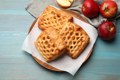 Delicious puff pastries and apples on light blue wooden table, top view