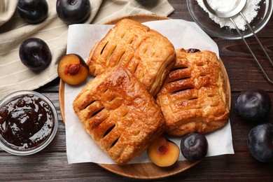 Photo of Delicious puff pastries, jam and plums on wooden table, top view