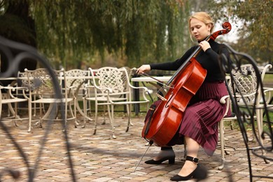 Photo of Beautiful young woman playing cello in park, space for text