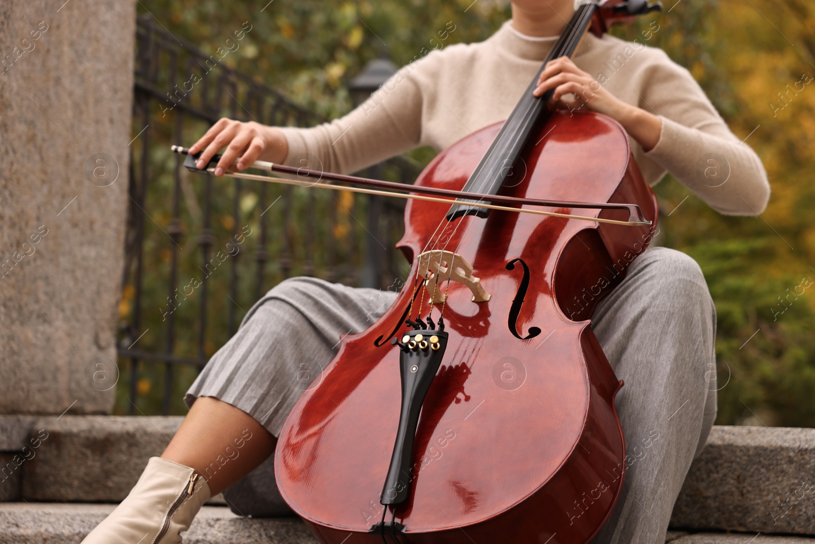 Photo of Young woman playing cello on stairs outdoors, closeup. Classic musical instrument