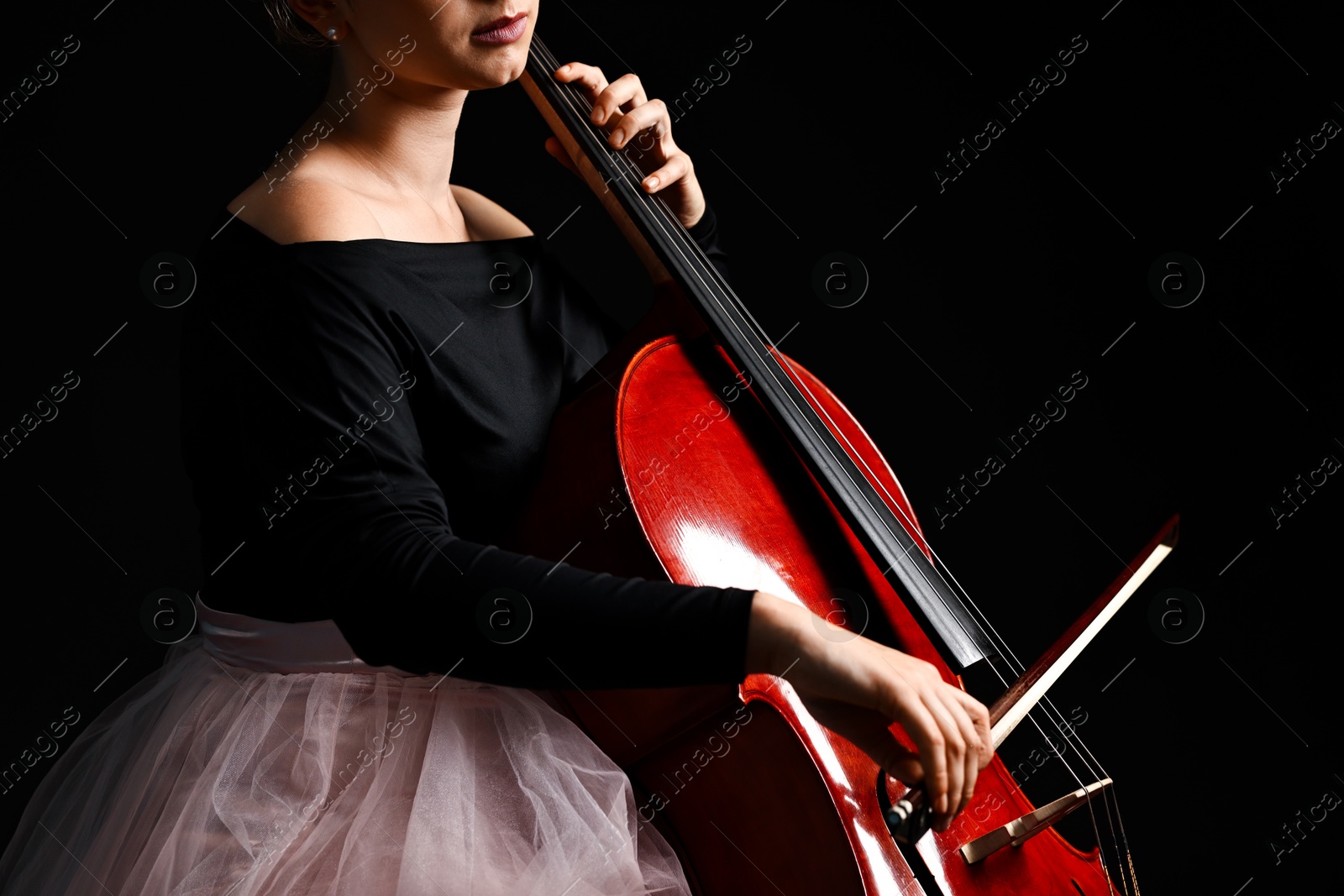 Photo of Young woman playing cello on black background, closeup