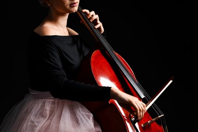 Photo of Young woman playing cello on black background, closeup