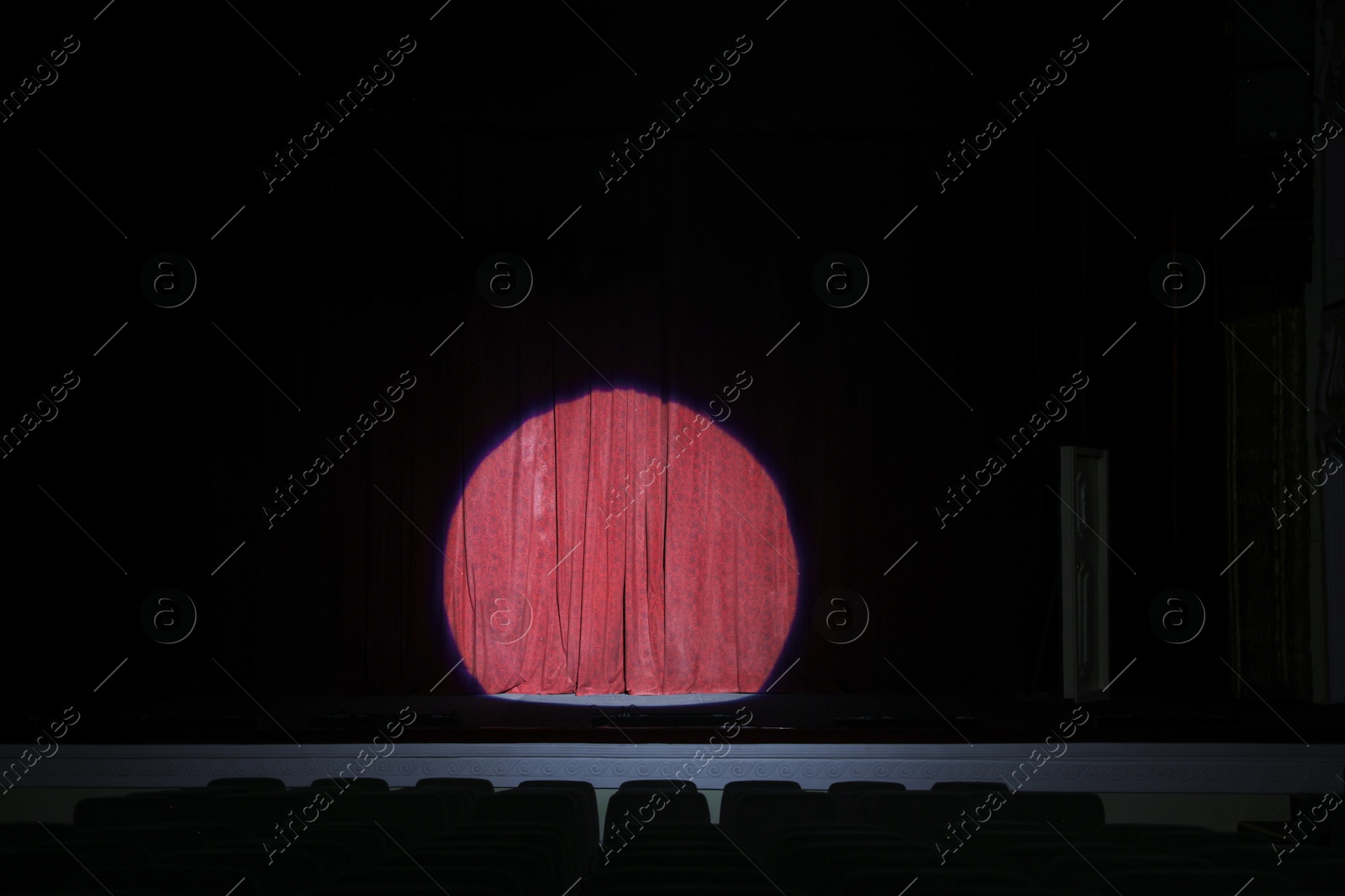 Photo of Spotlight illuminating closed red curtains on stage in theatre