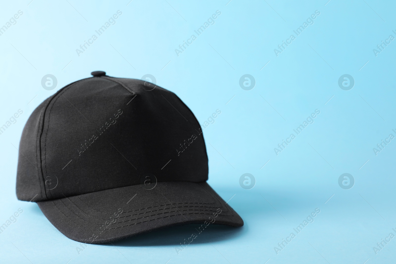 Photo of Stylish black baseball cap on light blue background. Mockup for design