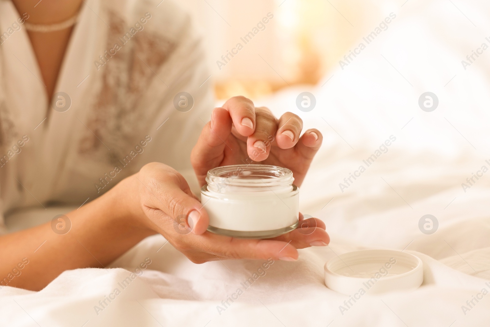 Photo of Woman with jar of cream on bed at home, closeup. Space for text