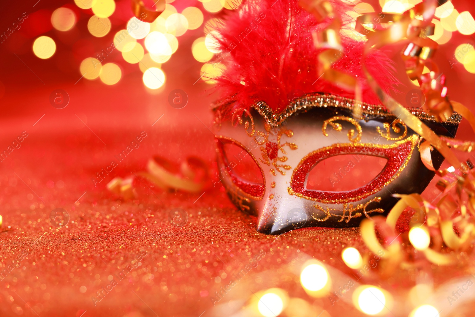 Photo of Beautiful carnival mask on shiny red background, closeup. Bokeh effect