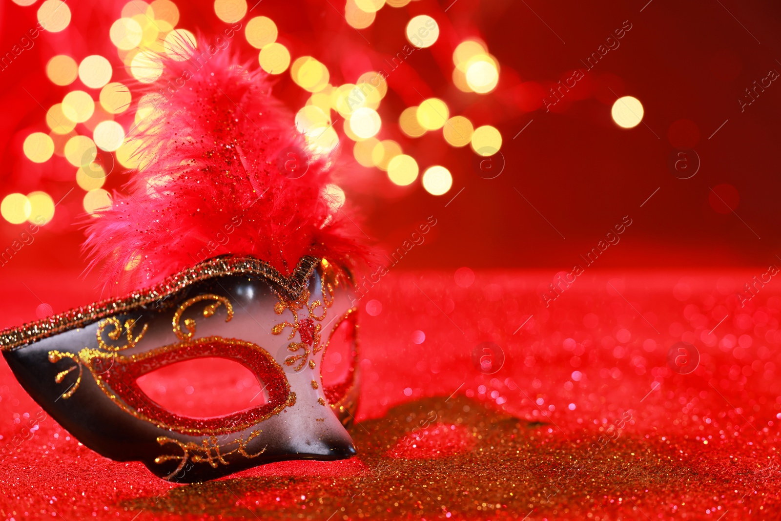 Photo of Beautiful carnival mask on shiny red background, bokeh effect. Space for text