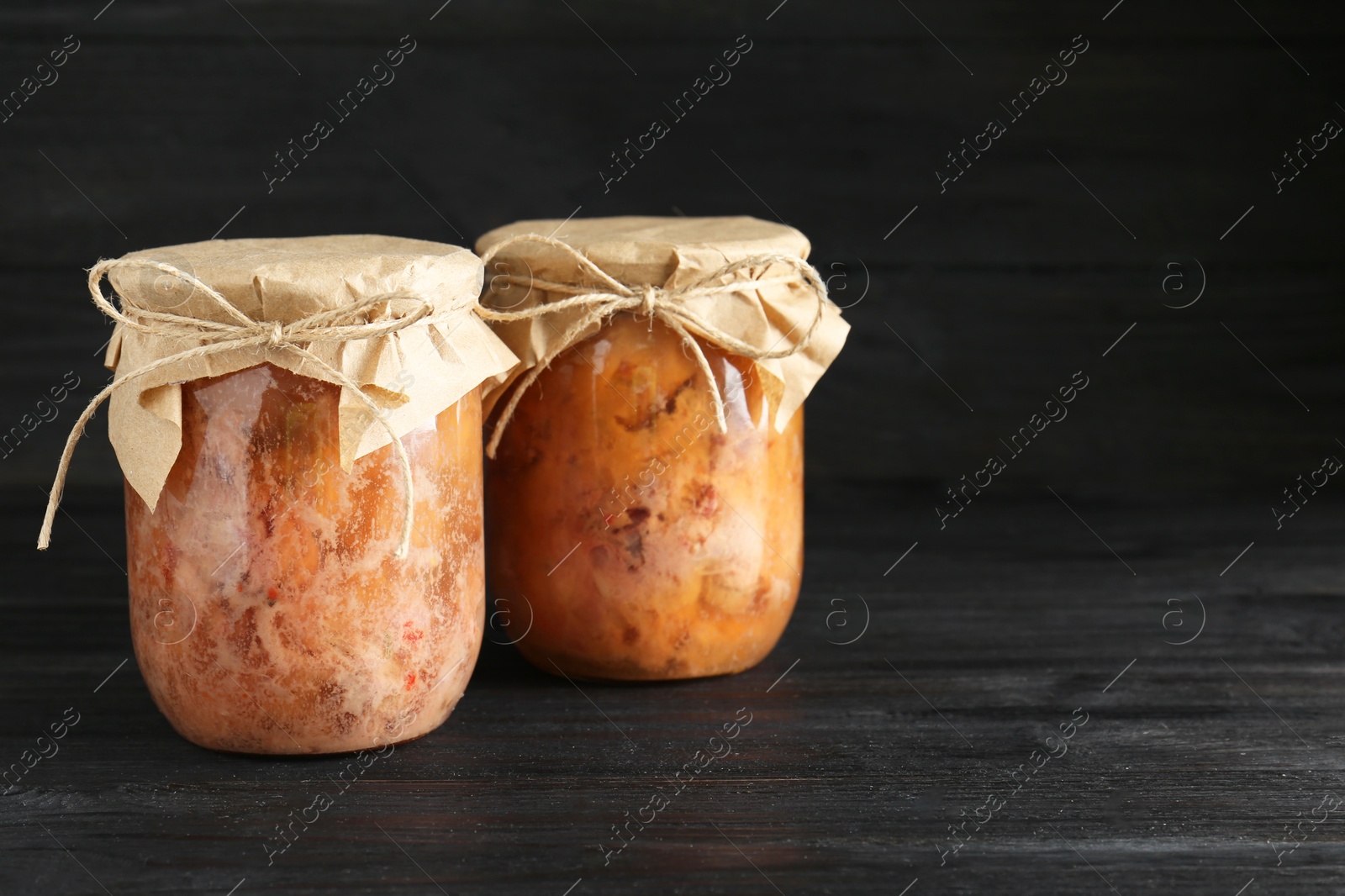 Photo of Canned meat in glass jars on wooden table, space for text