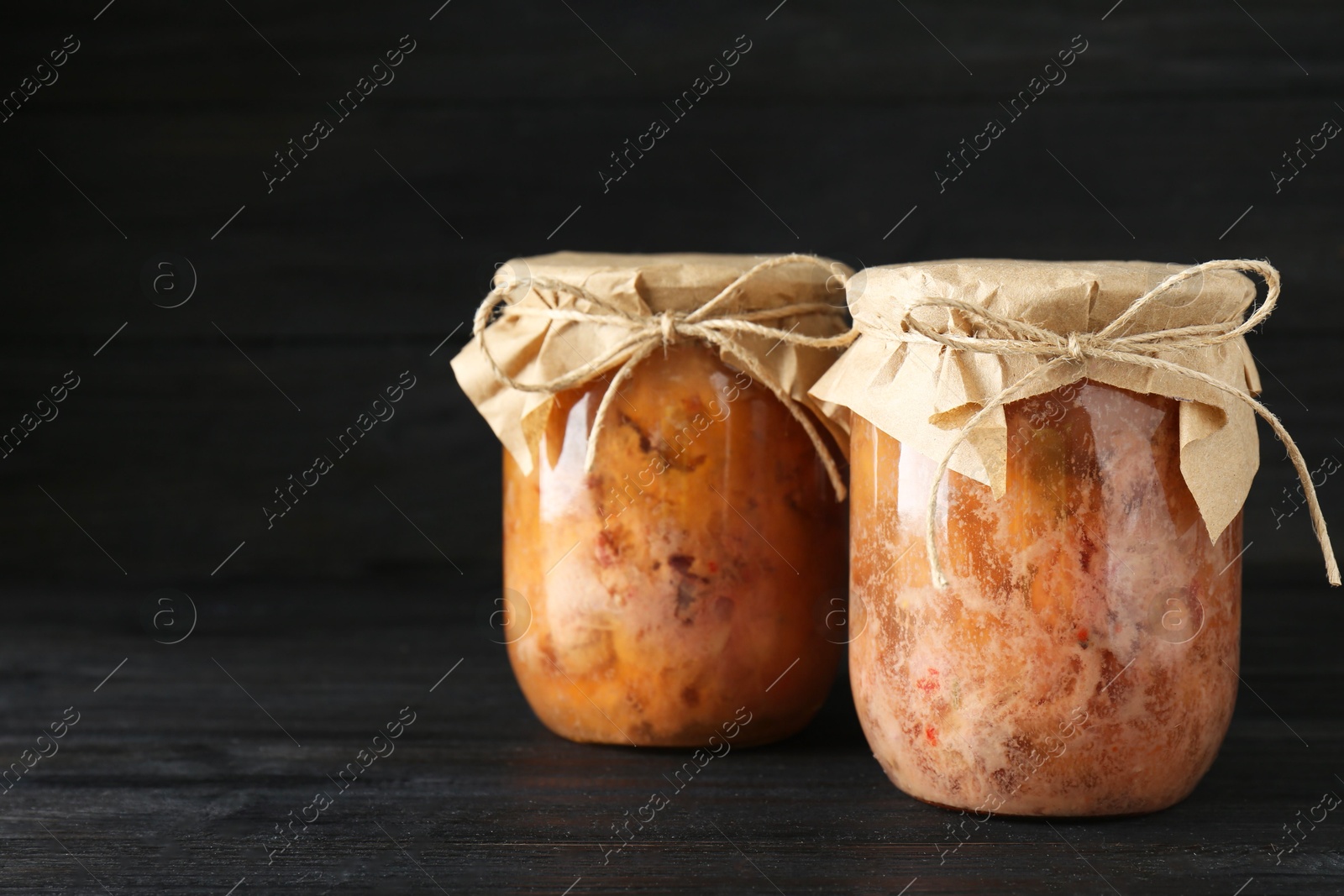 Photo of Canned meat in glass jars on wooden table, space for text