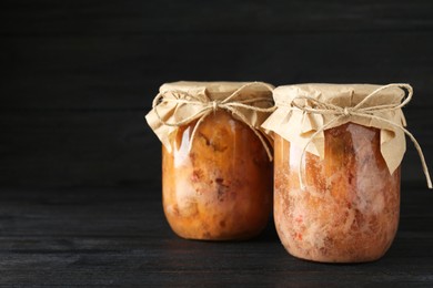 Photo of Canned meat in glass jars on wooden table, space for text