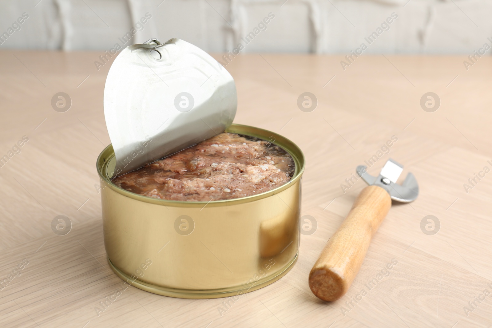 Photo of Canned meat in tin can and opener on wooden table, closeup