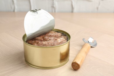 Canned meat in tin can and opener on wooden table, closeup