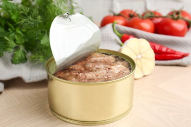 Canned meat in tin can and other products on wooden table, closeup